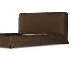 Lower side corner of bed slipcovered in coffee brown linen with slight fabric folds
