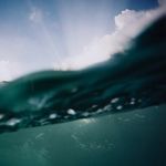 Close-up cropped look focusing on the wave crest and blurred water surface with sunlight filtering through