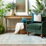 Room with rug laid out in front of wooden console table and dark green armchair accented with plush pillows