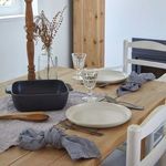 Seed grey square baker styled on wooden dining table with plates, glassware, and cloth napkins