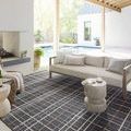 Plaid rug styled in a bright outdoor patio setting under a beige couch and near a fireplace