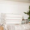 stack of cream-colored throws with black striped accents displayed on white shelf in cozy room setting