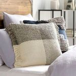 Styled pillow on bed surrounded by light gray bedding and wooden headboard in bedroom setting