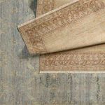 Folded rug corner revealing intricate border design in golden beige with purple accents