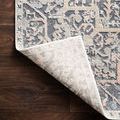 Lucia Rug corner folded over to reveal light-colored backside construction on wood flooring