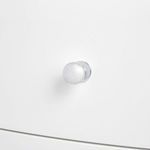 Chrome round drawer knob in close-up on white drawer front of side table