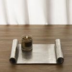 Brushed aluminium scroll tray on wooden surface with lit candle in glass holder styled