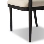 Close-up of the dark black wood leg and edge of the neutral seat cushion on Tova Dining Armchair