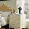 Side table with layered accessories lit by natural light from large window in bedroom setting