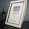 Frame displayed on dark surface with decorative black vase and textured wall background