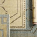 Stack of rugs in various muted tones including blue, beige, and patterns with geometric designs
