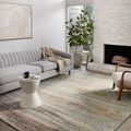Living room setting with rug placed between grey sofa and white chair near a fireplace.