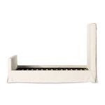 Close-up of wooden slat bed frame beneath natural linen slipcover base showing metal support structure