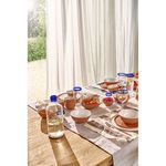 Carafe alongside matching blue-rimmed glasses and terracotta bowls styled on sunlit dining table with outdoor view