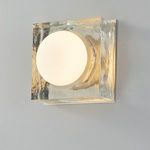 Square sconce illuminated with warm light through frosted globe central to hammered brass frame