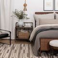 Bedroom setting with rug under nightstand and rattan bed frame with neutral bedding.