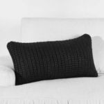 Black knit pillow shown angled on white couch, highlighting scale and outdoor setting