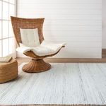 Rug laid out with wicker swivel chair and natural light showing subtle trellis pattern in soft tones