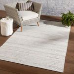 Eliza rug styled under a wicker armchair and white side table against brick wall on wood floor