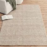 Chevron jute rug styled in a living room setting with sofa, wooden floor, book, and throw blanket