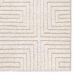 Detail of rug corner showing geometric lines converge to form a cross pattern in taupe on cream