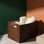 Chestnut leather tool box styled with cream knit throw inside, placed in corner with green and terracotta walls