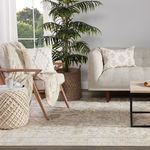 Rug in cozy setting with beige armchair, knitted throw, decorative pillows, and tall green plant.