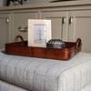 Tray placed on soft striped ottoman with picture frame and decorative container in cozy living space