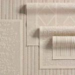 Repeated stack of multiple neutral patterned outdoor rugs in different woven geometric textures