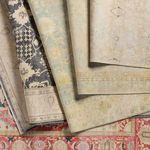 Stack of rugs highlighting Lovato Floral Blue/Green Rug’s faded floral pattern and color palette among other global rug de...