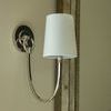 Close view of sconce mounted by large mirror showing polished metal arm and white linen shade in soft lighting