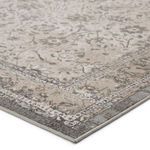 Close-up angled corner view showing woven texture and detailed floral border in gray and beige tones