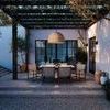 Outdoor evening scene showing Bohen sconces lit on white walls with garden furniture beneath pergola