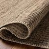 Close-up of curled corner highlighting thick woven texture and natural fibers of rug