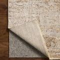 Rug corner lifted to reveal woven backing and thin gray rug pad underneath on hardwood floor