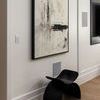 side angle of artwork in minimalist room showing black sculptural chair beneath painting