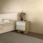 Side view of nightstand in bedroom setting next to upholstered bed on wood floor