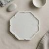 White marble lotus tray styled on beige fabric surface with small white bowl, smooth stone, and gray linen