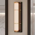 Close-up of illuminated Blaine sconce mounted on neutral wall with brass and bronze finishes