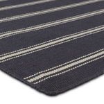 Angled close-up of flatwoven navy rug with ivory thin and thick stripes showing fabric texture