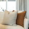 Rust Bedford pillow next to large striped ivory pillow on a light sofa by window