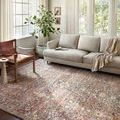 Rug styled in a bright living room with beige sofa, wood chair, and natural light through large windows