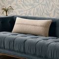 Harvey Ivory Pillow placed on a dark blue velvet tufted sofa against a wallpapered wall