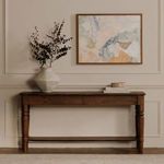Esti painting hung above a wooden console table with a white vase and decorative objects
