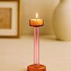 Glass candle holder lit with a small candle on top, shown on beige surface with blurred background