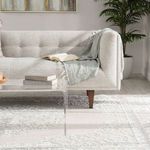 Side-angle of sofa leg on rug showing texture contrast and part of acrylic coffee table