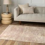 Rug laid on wood floor in a living room setting with a beige sofa, cream pillows, and a side table lamp