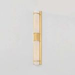 Sconce illuminated with warm light against grey wall emphasizing brass finish and glass texture