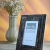 Frame placed on textured surface with warm yellow-orange background and decorative vase in background