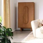 Cabinet styled in bright living room corner beside white armchair, plant, and textured rug